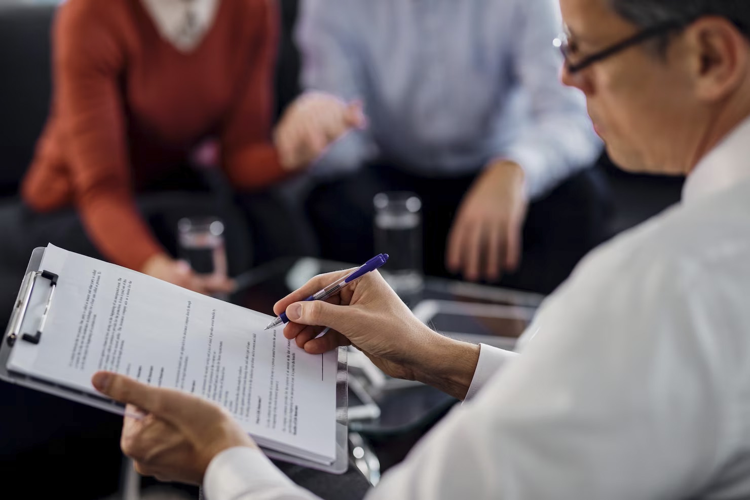 Primer plano de un agente revisando un contrato de arrendamiento mientras se reúne con sus clientes.